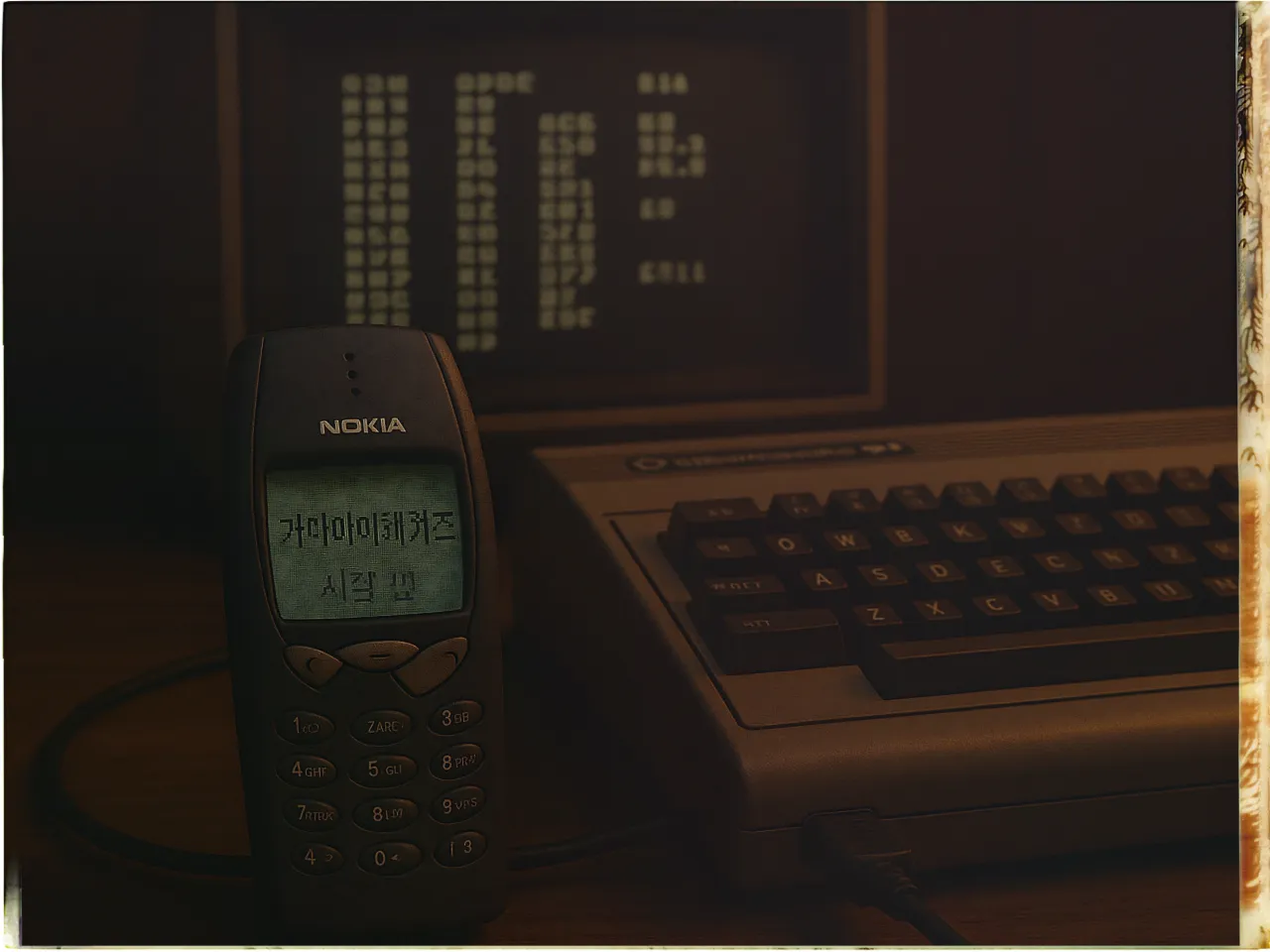 A vintage Nokia mobile phone with a green-lit screen displaying a text is placed on a wooden surface. To the right, there is a retro computer keyboard attached to a Commodore 64, an early model home computer. In the background, a monitor displays text in a blocky, monochrome font, adding to the nostalgic feel of the setting. The overall lighting is dim, evoking a sense of retro technology.