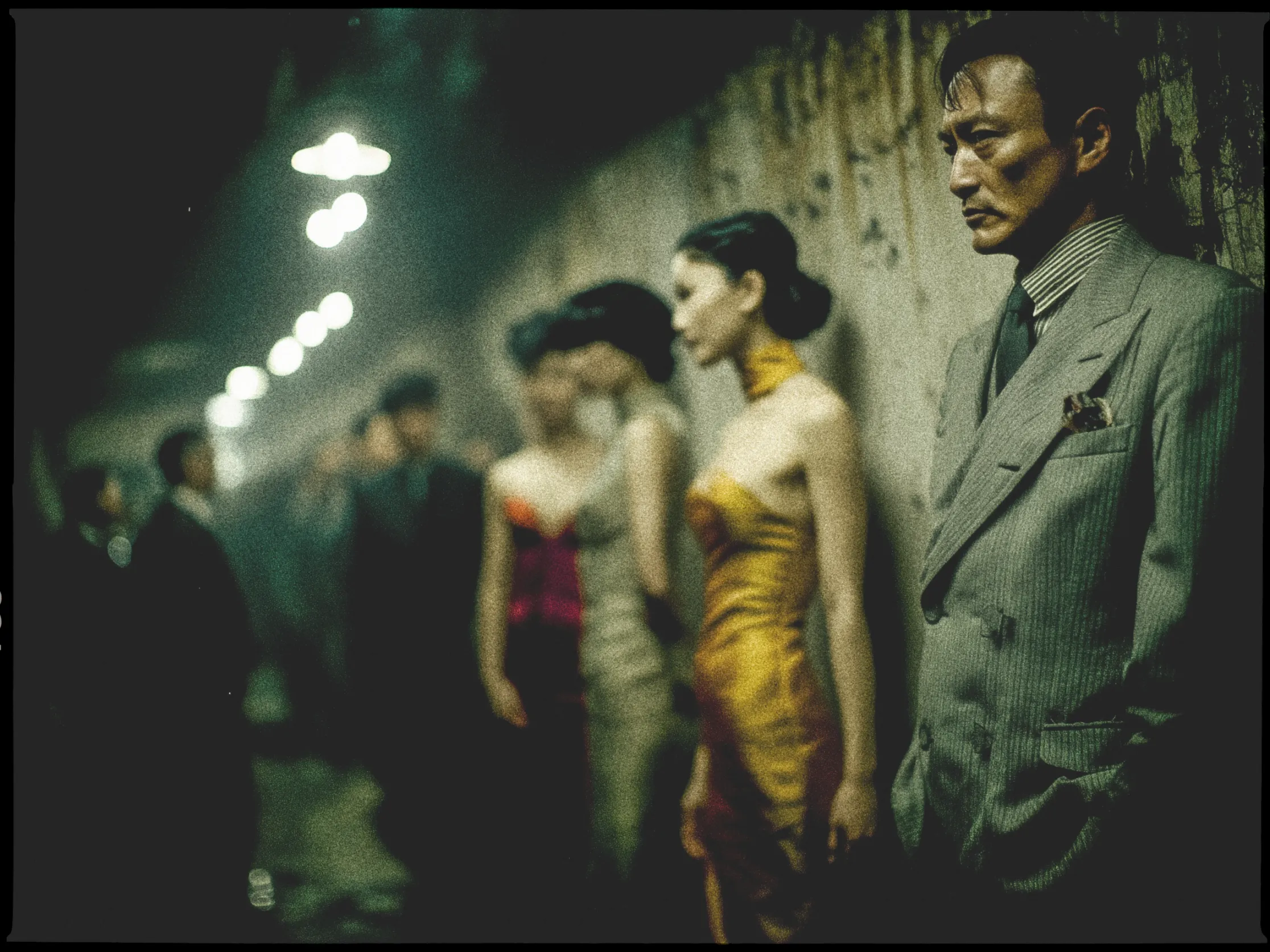 In a dimly lit, atmospheric scene, a group of elegantly dressed individuals stand against a textured wall. In the foreground, a man in a sharp gray pinstripe suit with a pocket square looks pensive, with his hands in his pockets. Beside him, a woman in a striking gold strapless dress stands with her hair styled up. The background is filled with more people, slightly out of focus, wearing formal attire. Overhead lights create a moody ambiance as they recede into the distance, casting a subtle glow on the scene.