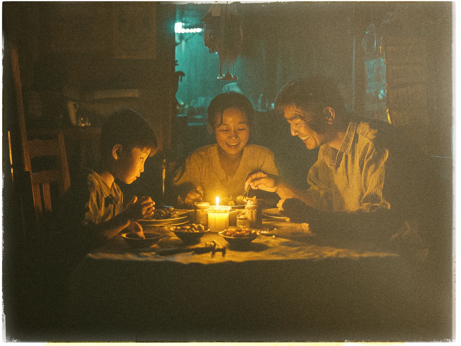 A family of three sits around a table in a dimly lit room, illuminated by the warm glow of a single candle. The child on the left, wearing a light-colored shirt, looks intently at the food in front of them. In the center, a woman smiles warmly, engaging with the others. On the right, a man is also smiling, creating an atmosphere of joy and togetherness. The table is set with various dishes, suggesting a shared meal. The background is softly blurred, with hints of kitchen elements, adding to the cozy and intimate ambiance.