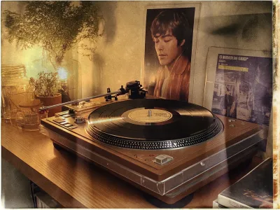 A warm, vintage-styled image featuring a wooden turntable with a black vinyl record on it, positioned prominently on a wooden shelf. The record's label is partially visible. To the left, there are small potted plants and decorative glass jars, contributing to a cozy ambiance. Behind the turntable, a framed photograph of a man with closed eyes is displayed. To the right, a partially visible album cover shows additional artwork. The scene is softly lit, casting gentle shadows and evoking a nostalgic atmosphere.